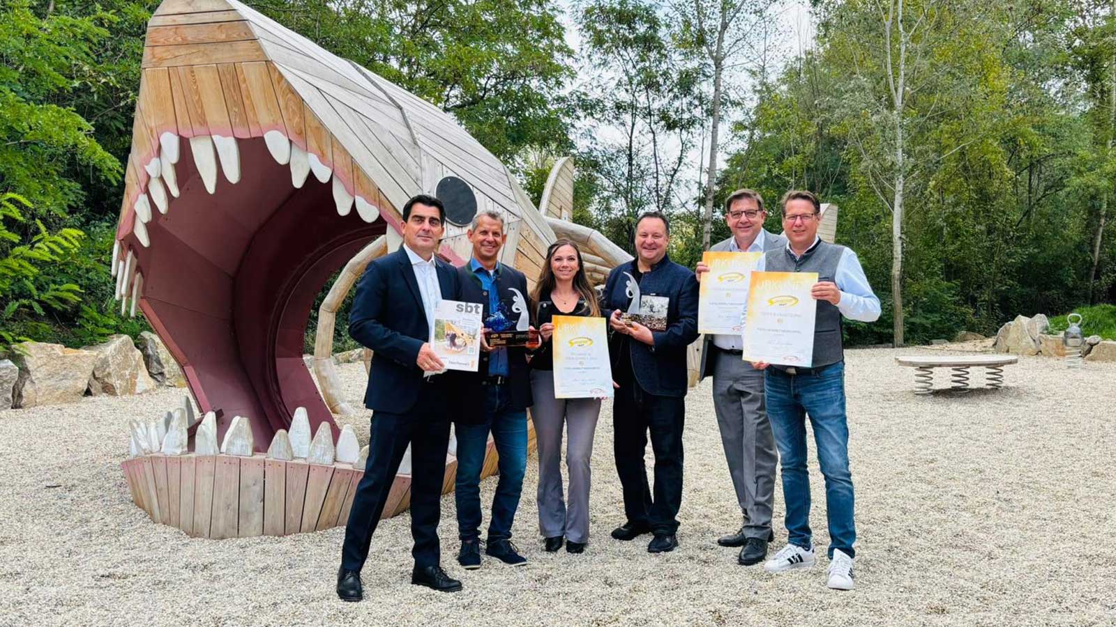 Representatives of Fossil World Weinviertel holding awards in front of the giant shark attraction.