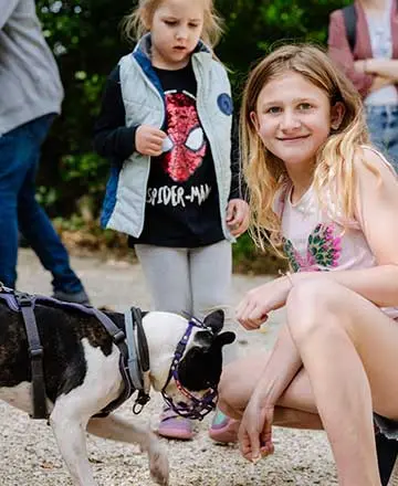 Kinder im Außengelände der Fossilienwelt, eines streichelt einen Hund.