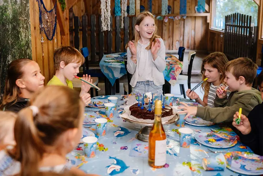Kinder feiern einen Geburtstag an einem bunt gedeckten Tisch in der Fossilienwelt.