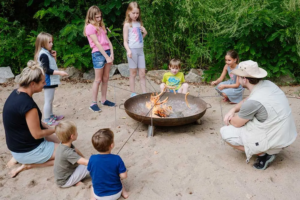 Kinder grillen Würstel am Lagerfeuer während eines Geburtstagsprogramms in der Fossilienwelt.