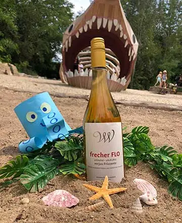 Flasche und Deko im Sand vor dem großen Haifischmodell der Fossilienwelt.