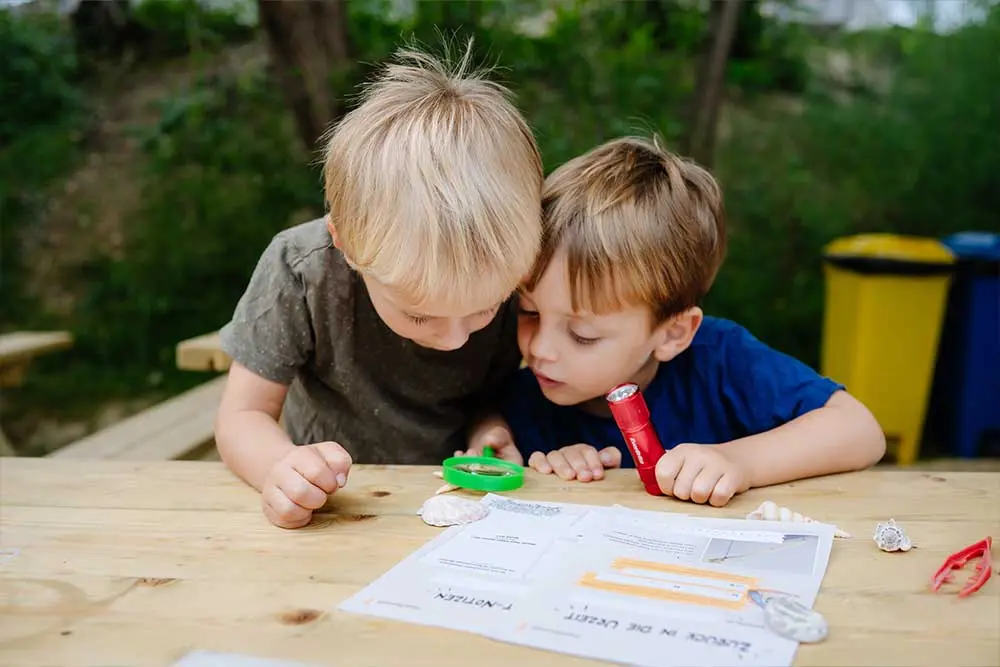 Kinder untersuchen Muscheln und Fundstücke mit Lupe und Licht in der Fossilienwelt.