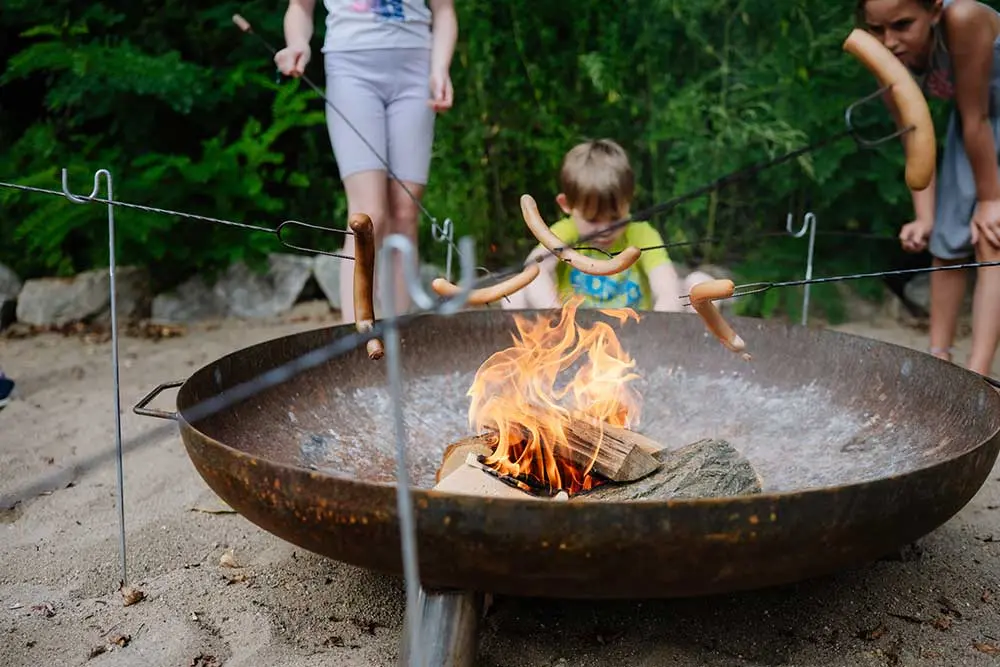 Kinder grillen Würstel am Lagerfeuer während einer Gruppenaktivität in der Fossilienwelt.
