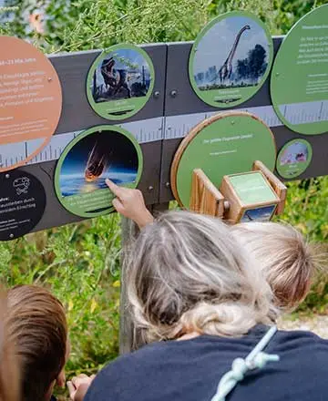 Kinder betrachten eine Infotafel zu Dinosauriern und Meteoriten in der Fossilienwelt