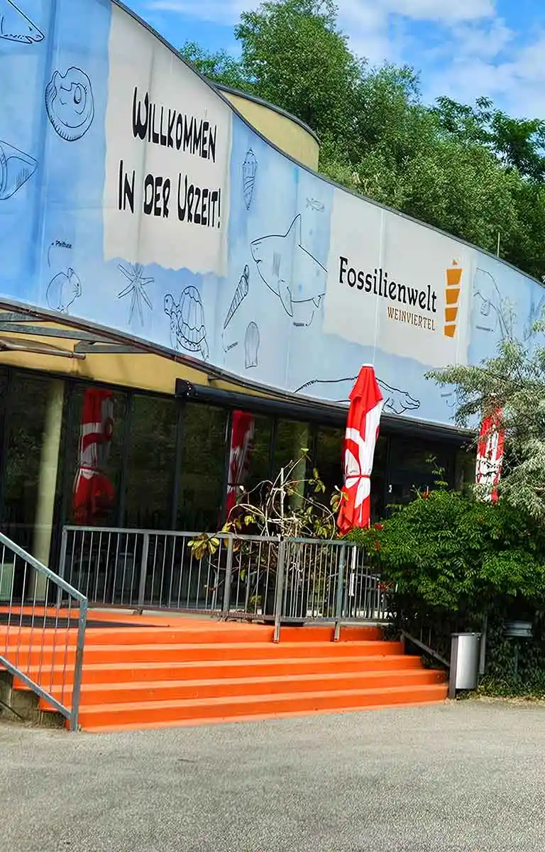 Eingangsbereich der Fossilienwelt Weinviertel mit Willkommensbanner und Aussichtsturm im Hintergrund